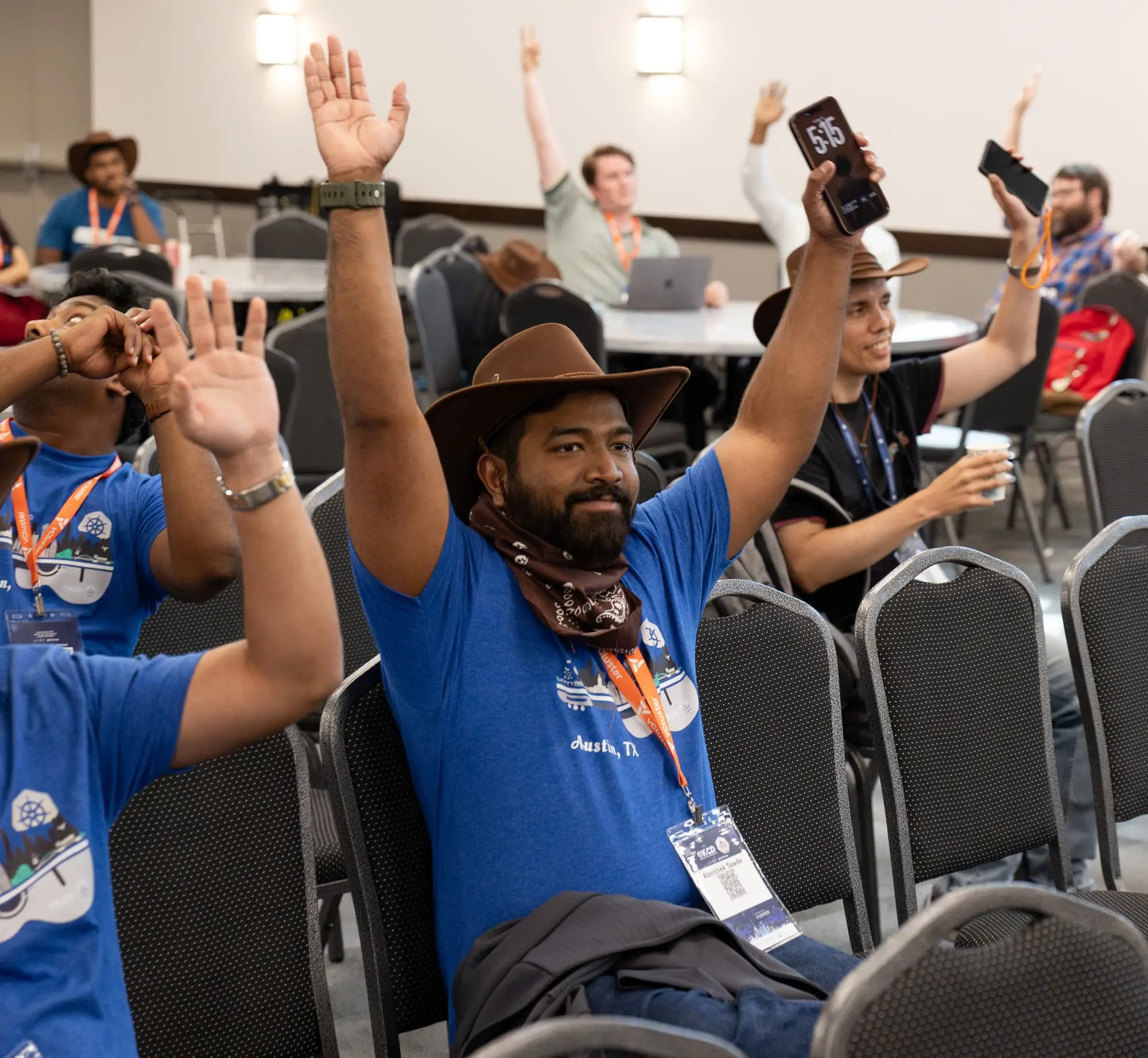 An attendee in a cowboy hat and bandana raises an arm for the closing raffle, with more raised hands behind.