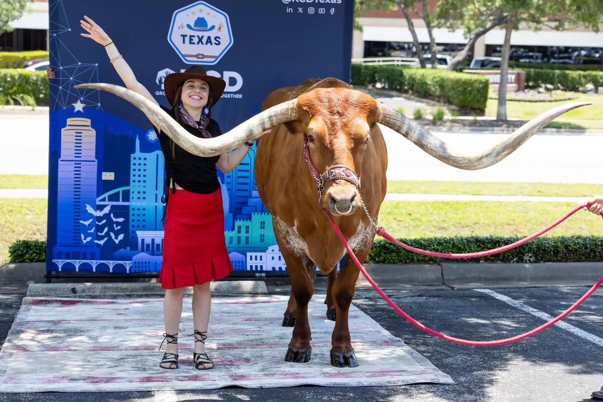 An attendee in a cowboy hat raises an arm beside a Texas longhorn with wide horns, in front of the KCD Texas backdrop.
