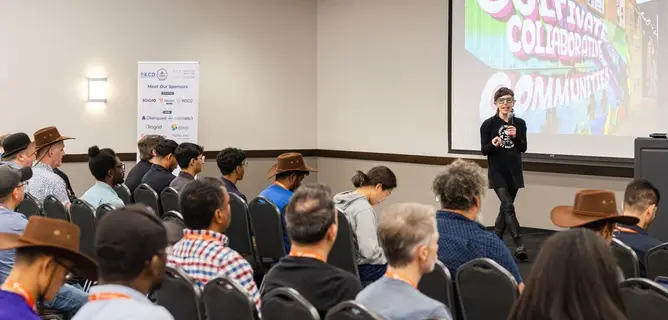 KCD Texas 2026: Ian Coldwater gives a keynote to a full room of attendees, many in cowboy hats.