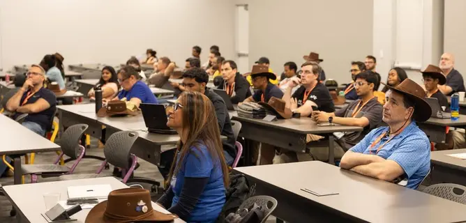 KCD Texas 2026: a packed afternoon session of attendees at tables with laptops listens to a talk.